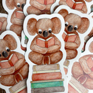 Sticker of a Koala Reading a Book on a stack of books